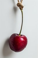 Fresh ripe red cherry with water drops and green stem on white background, macro shot showing natural texture and juicy appearance.