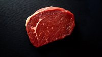 Fresh raw beef tenderloin steak with marbling texture on black stone background, close up view of premium cut meat for cooking and grilling.