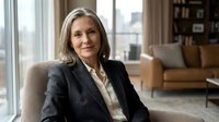 Confident mature Caucasian businesswoman in dark suit sitting in modern office interior, professional executive portrait for corporate communications.