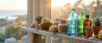 Natural skincare products and essential oils arranged on wooden windowsill with warm sunlight and plants creating spa atmosphere for wellness routine.