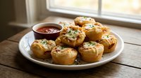 Golden baked pastry bites filled with savory ingredients, garnished with fresh herbs, served on white plate with dipping sauce by sunny window.