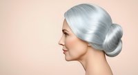 Woman with silver hair styled in a low bun, profile view against neutral background. Suitable for beauty, aging, hair care, and cosmetics marketing materials.
