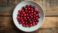 Fresh ripe cranberries in ceramic bowl on rustic wooden background, top view. Natural organic berries for cooking seasonal dishes and desserts.