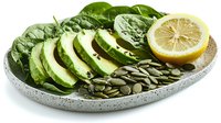 Fresh sliced avocado with baby spinach leaves, pumpkin seeds and lemon on gray ceramic plate, healthy vegetarian food composition on white background.
