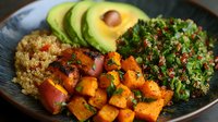 Healthy quinoa bowl with roasted sweet potato, fresh avocado slices and herb tabbouleh salad on dark plate for nutritious meal planning and clean eating lifestyle.