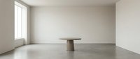Minimalist interior space with round pedestal table and concrete floor, modern gallery or showroom setting with natural light from window.