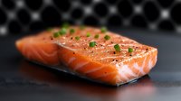Fresh raw salmon fillet seasoned with black pepper and chopped chives on dark background, close up view with selective focus for food photography.