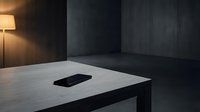 Minimalist workspace with smartphone on white table, dark walls, and warm lamp lighting for modern office design concepts.