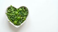 Fresh green microgreens in heart-shaped bowl on white background for healthy eating and nutrition concepts.