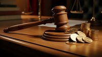 Wooden gavel and golden coins on judge desk with scales of justice in background for legal financial litigation and court proceedings.