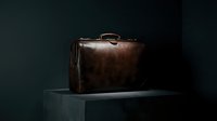 Vintage dark brown leather briefcase on a pedestal against a dark background, showcasing classic craftsmanship and timeless elegance.