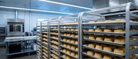 Commercial bakery production line with fresh bread loaves on metal racks in modern industrial kitchen facility for food manufacturing business.