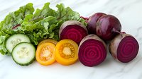 Fresh sliced vegetables on marble background - cucumber rounds, yellow tomato, red beets with circular pattern, and green lettuce leaves arranged in row.