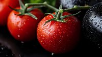 Fresh red and black tomatoes with water drops on dark background, macro shot with selective focus. For food photography and healthy eating concepts.