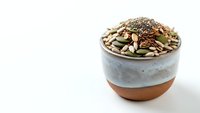 Mixed seeds and nuts in ceramic bowl on white background for healthy snacking and cooking ingredients.