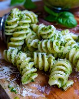 Fusilli pasta with fresh basil pesto sauce and grated parmesan cheese on wooden cutting board, close up view of traditional Italian cuisine preparation.