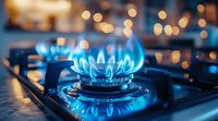 Blue gas stove flame burning on modern kitchen cooktop with bokeh lights in background, close up view showing energy consumption and cooking concept.