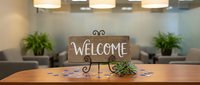 Rustic wooden welcome sign on metal easel with succulent plant on modern dining table in contemporary home interior with pendant lighting and green plants.