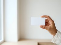 Close-up of hand holding blank white card in bright interior space, suitable for business presentations, marketing mockups, and promotional designs.