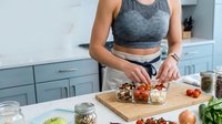 Young woman preparing healthy breakfast bowl with granola, berries and yogurt in modern kitchen. Nutritious morning meal preparation concept.