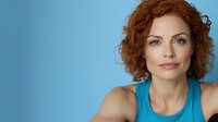 Professional redhead woman with curly hair in blue tank top against matching background for business and lifestyle marketing campaigns.