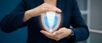 Professional businesswoman in dark suit protecting glowing blue security shield symbol with hands, representing cybersecurity and data protection services.