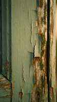 Weathered green paint peeling from aged wooden surface with rust stains and decay, showing deterioration and abandonment for backgrounds, textures, and grunge design elements.
