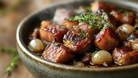 Caramelized pork belly chunks with pearl onions and fresh thyme served in rustic ceramic bowl, close-up shot showing glossy meat texture and aromatic herbs.