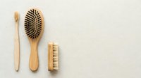 Eco-friendly bamboo hair care tools including toothbrush, paddle brush and nail brush arranged on neutral background for sustainable beauty routine.
