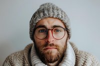 Close up portrait of bearded Caucasian man wearing knit beanie and round glasses looking at camera with gentle expression. Winter casual style.