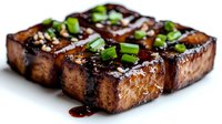 Grilled tofu steaks with teriyaki glaze and fresh green onions on white background, isolated plant-based protein for healthy cooking and vegetarian recipes.