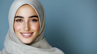 Young Middle Eastern woman wearing light gray hijab smiling warmly against blue background, showcasing natural beauty and confidence in modern portrait.