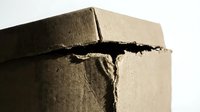 Damaged cardboard box with torn edges and cracks showing wear from shipping or storage on white background.
