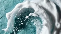 Aerial view of turquoise ocean waves with white foam and bubbles creating natural patterns on crystal clear tropical water surface.
