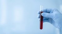 Medical professional in blue latex gloves holding test tube with red blood sample for laboratory analysis and diagnostic testing in clinical setting.