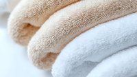 Soft folded towels in beige and white colors with textured terry cloth surface, creating gentle waves and shadows. Clean fresh bathroom linens for spa and hotel.