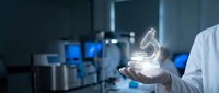 Young male scientist in white lab coat holding glowing microscope hologram in modern laboratory with equipment and monitors, representing medical research and biotechnology innovation.