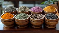 Aromatic spices and seasonings in wooden bowls arranged in rows, including turmeric, black pepper, pink salt and dried herbs on rustic wooden table surface.