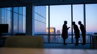 Business professionals silhouetted against floor-to-ceiling windows overlooking cityscape at dusk, suitable for corporate, leadership, and teamwork concepts.