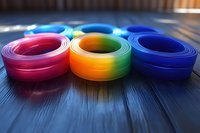 Vibrant rolled ribbons in red, rainbow gradient, and blue colors arranged on dark wooden surface with selective focus and soft bokeh effect background.