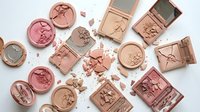 Luxury makeup collection featuring rose gold and pink eyeshadow palettes with broken powder cosmetics scattered on white background for beauty.