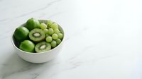 Fresh green kiwi fruits and grapes arranged in white bowl on marble surface, healthy organic produce for nutrition and wellness content.
