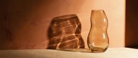 Amber glass vases with organic wavy shapes casting warm shadows on neutral surface, suitable for home decor and interior design projects.