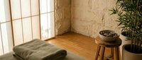 Zen meditation corner with green cushion, wooden stool, singing bowl and bamboo plant in minimalist room with natural light for mindfulness practice.