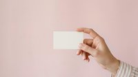 Young adult with medium skin tone holding blank white business card against soft pink background for branding and corporate identity projects.