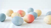 Colorful speckled Easter eggs in pastel blue, pink and cream tones scattered on white surface for spring holiday celebration and seasonal decoration.