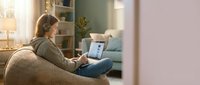 Young woman working on laptop computer while sitting comfortably on modern sofa in cozy living room interior during evening hours for remote work.