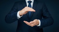 Professional businessman in dark suit making protective gesture with hands for insurance and security concepts.