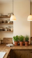 Modern kitchen interior with pendant lights, wooden shelves, ceramic dishes and fresh herbs in terracotta pots on rustic wooden counter.