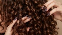 Woman with beautiful brown curly hair touching her natural ringlets with manicured hands showing healthy hair texture and volume for beauty care.